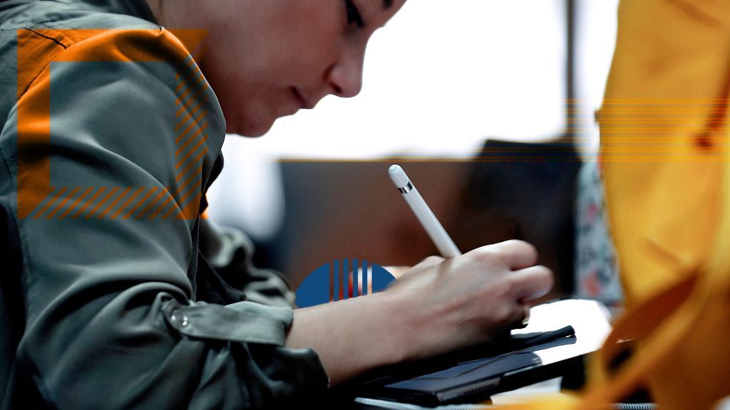 étudiante qui tient un stylo blanc et qui écrit sur son bureau
